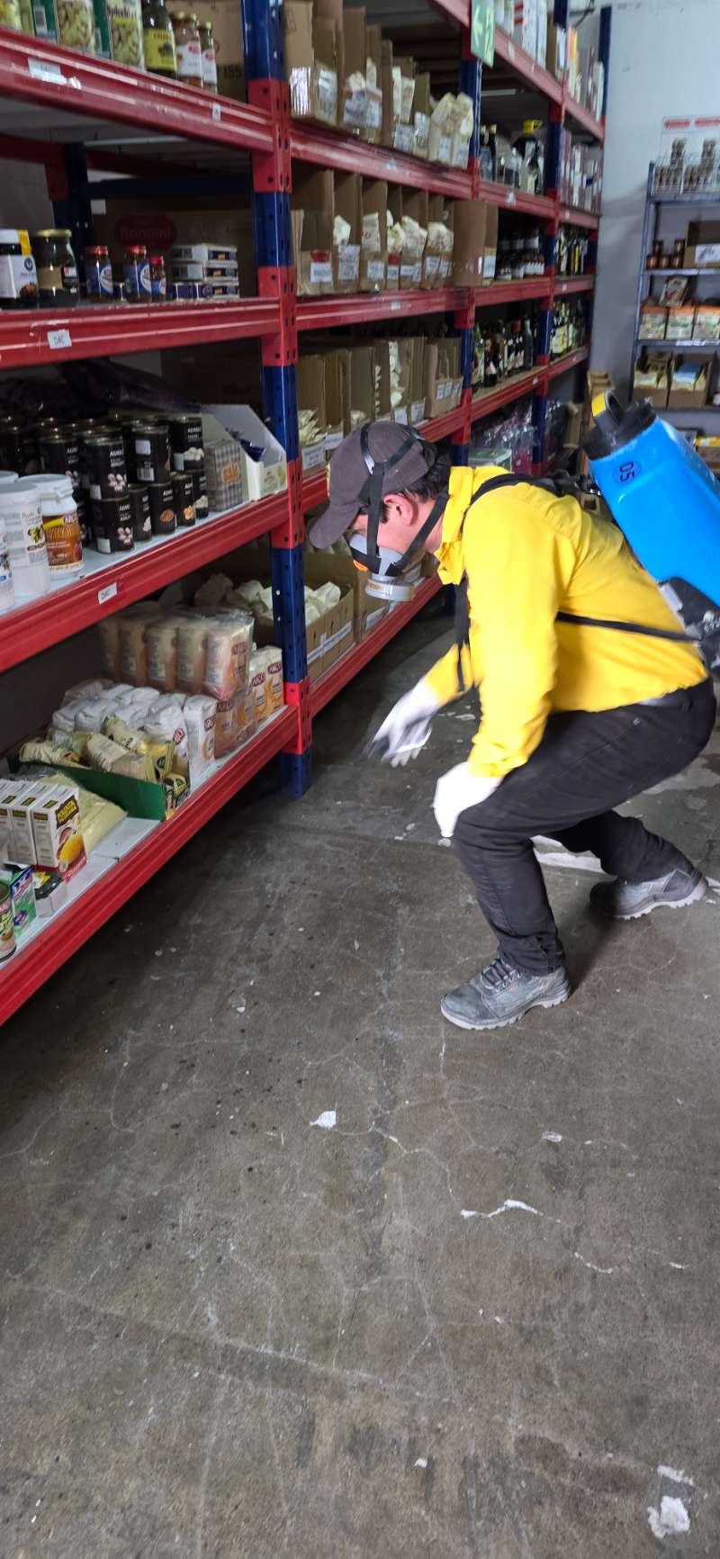 EcoPlagas technician in respirator and uniform treating a corner store