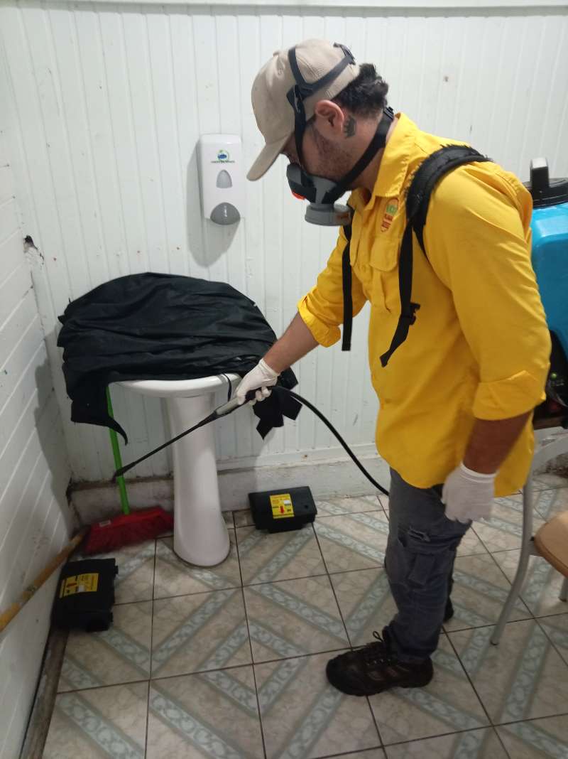 EcoPlagas technician in respirator, cap and gloves treating a commercial restroom