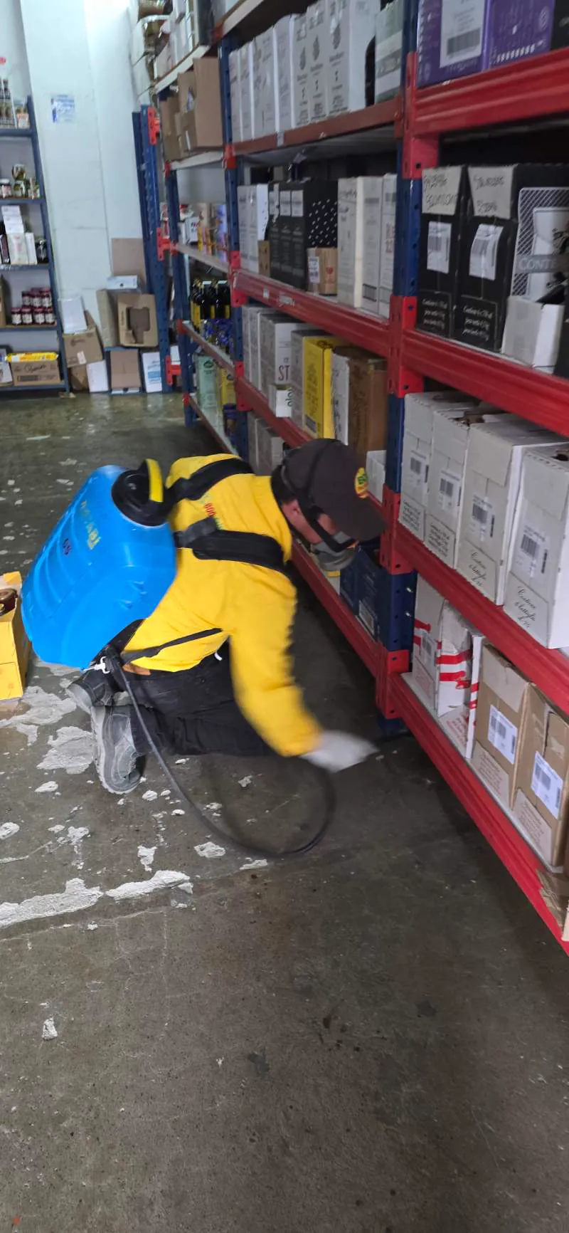 Técnico de EcoPlagas aplicando aspersión residual bajo estanterías de una bodega