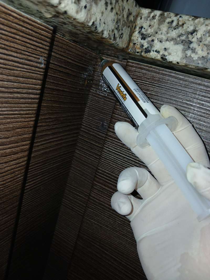 Application de gel anti-cafards à la seringue dans une fissure de meuble de cuisine