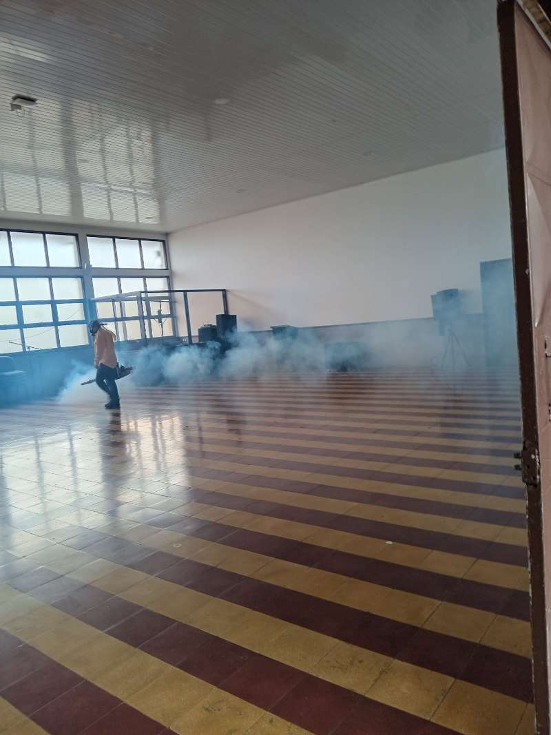 EcoPlagas technician fogging a large institutional hall with visible mist