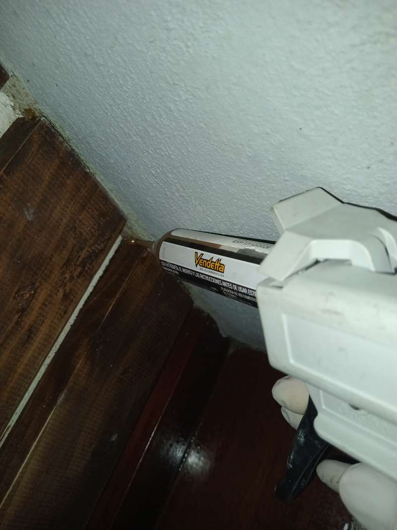 Pistolet doseur appliquant un gel professionnel anti-cafards à la jonction entre le mur et le meuble